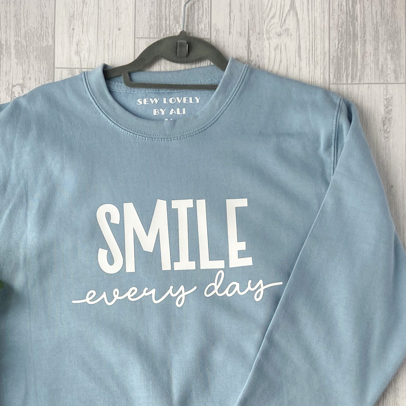 Ice blue crew neck sweatshirt with white wording that reads 'Smile Every Day'.