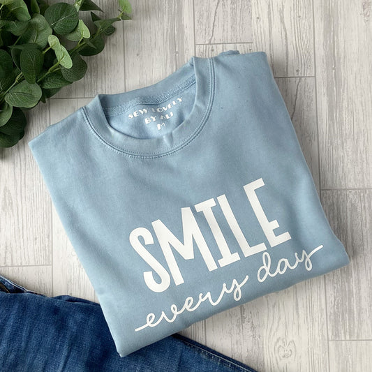 Ice blue crew neck sweatshirt with white wording that reads 'Smile Every Day'.