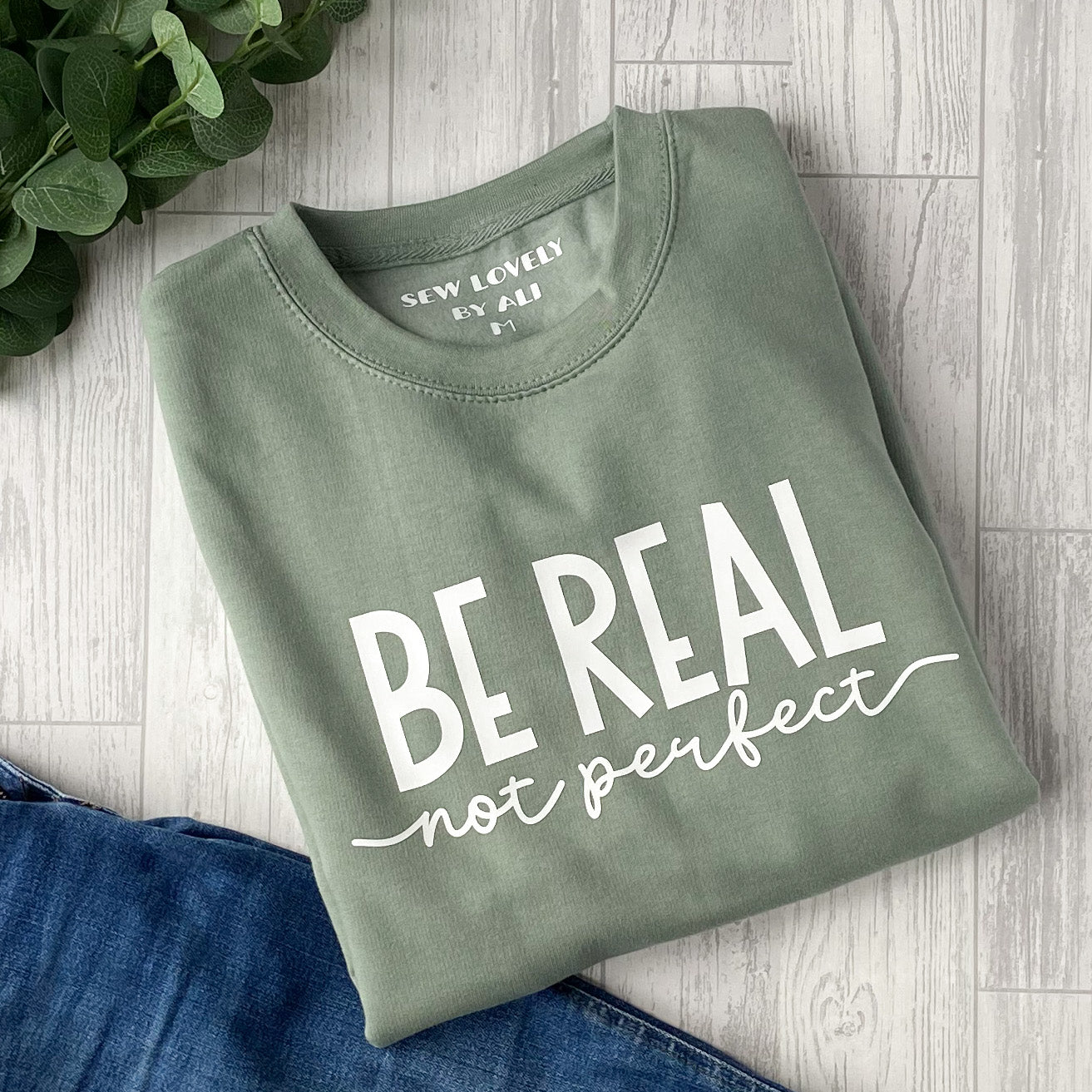 Dusty green crew neck sweatshirt with white wording that reads 'Be Real Not Perfect'.