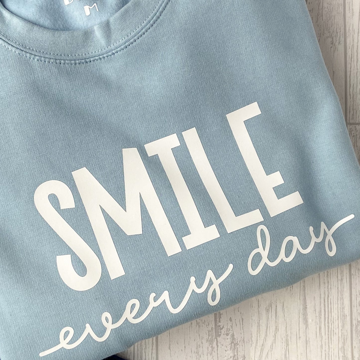 Ice blue crew neck sweatshirt with white wording that reads 'Smile Every Day'.